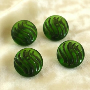 May include: Four round, green glass buttons with a swirled, dark green design. The buttons are evenly spaced and appear to be vintage or antique. The buttons are on a cream-colored fabric.