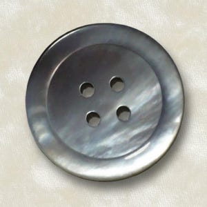May include: A round, four-hole button with a smooth, iridescent dark gray surface. The button features a recessed center area and a wide, slightly raised outer rim, displaying a natural, pearlescent sheen that reflects light across its surface.