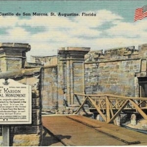 May include: Vintage postcard of Fort Marion National Monument in St. Augustine, Florida. The image shows the entrance to the fort, with a wooden bridge leading to the stone structure. An American flag flies in the background.