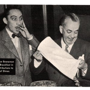 May include: Black and white photograph of two men in suits. One man is surprised, touching his face, while the other holds a white cloth. Text in the image reads: Mischa Auer, Tom Breneman and 523,000 Breakfast in Hollywood contributions to the March of Dimes.