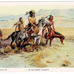 May include: Vintage postcard illustration depicting Native American warriors on horseback in a desert landscape. The artwork features three riders in the foreground, with others in the distance. The text "IN THE ENEMY COUNTRY" is at the bottom.
