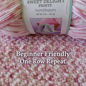 May include: A close-up of a skein of Baby Bee Sweet Delight Prints yarn in the color "bumblegum." The yarn is pink and white. The image also shows a crocheted swatch in a textured pattern. Text on the label reads "Beginner Friendly One Row Repeat."