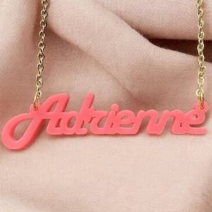 Könnte beinhalten: Eine rosafarbene Acryl-Halskette mit dem Namen "Adrienne" in Kursivschrift.