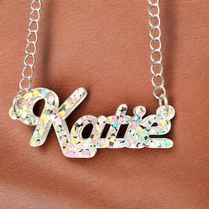Peut inclure: Un collier en argent avec un pendentif en forme de plaque de nom scintillant et iridescent qui dit "Katie".