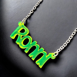 May include: A silver chain necklace with a green and yellow acrylic pendant that says "Romm".
