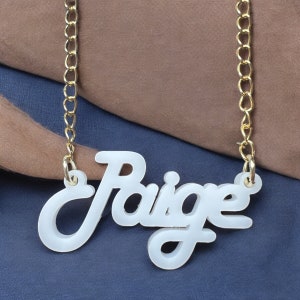 Könnte beinhalten: Eine weiße Acryl-Halskette mit einer goldenen Kette und dem Namen "Paige" in kursiv.