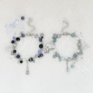 May include: Two beaded bracelets with silver chains and charms. One bracelet has a microphone charm, the other a guitar. Both have star, heart, and musical note charms, with blue, black, and clear beads.