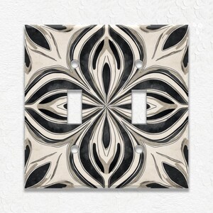 May include: A decorative light switch cover with a floral design. The cover features a symmetrical pattern in black, gray, and off-white. It has two switch openings and four screw holes for installation. The design is reminiscent of a watercolor painting.
