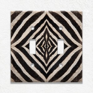 May include: A decorative double light switch cover featuring a zebra print design. The cover has a square shape with two toggle switch openings and four screw holes. The zebra pattern is black and white.