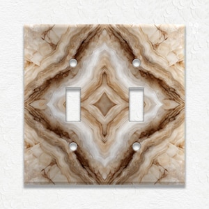 May include: A double light switch cover with a marbled pattern in shades of brown, beige, and white. The cover has two light switch openings and four screw holes. The design is symmetrical, with a diamond shape in the center.