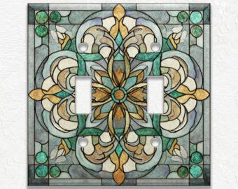 May include: A decorative light switch cover with a stained glass design. The cover features a symmetrical floral pattern in shades of teal, gold, beige, and white. The design includes two switch openings and is framed by a teal border.