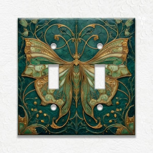 May include: A decorative double light switch cover featuring a butterfly design. The butterfly has green and gold wings with intricate details, set against a teal background with floral accents. The cover has two switch openings and white screws.