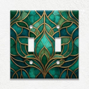 May include: Decorative double light switch cover with a stained glass design. The cover features a teal, green, and gold color scheme with a floral pattern. The light switches are white.