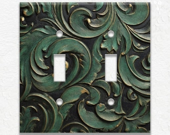 May include: A decorative double light switch cover with a detailed, raised floral design. The cover features a dark green and gold color scheme with a black background. The design includes two switch openings and four screw holes.