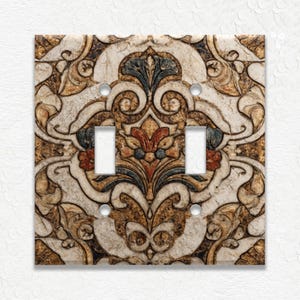 May include: Decorative double light switch cover with an ornate, vintage-style design. The cover features a beige background with a detailed pattern in shades of brown, red, and blue. The design includes floral and scroll elements.