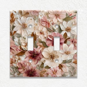 May include: A decorative light switch cover featuring a floral design. The cover has two switch openings and is adorned with a textured pattern of white, pink, and mauve flowers with green leaves. The overall aesthetic is reminiscent of a painted canvas.