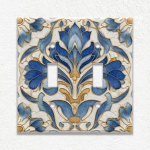 May include: A decorative light switch cover with a floral design. The cover features a white background with blue and gold floral patterns. It has two switch openings and a square shape.