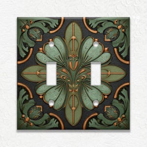 May include: Decorative double light switch cover with a green and bronze floral design on a black background. The cover features a symmetrical pattern with intricate details and a textured appearance.