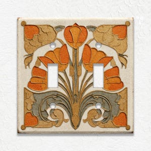 May include: A decorative double light switch cover with an Art Nouveau floral design. The cover features orange, gold, and gray stylized flowers and leaves on a cream-colored background. The cover has two switch openings and four screw holes.
