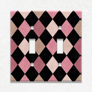 May include: A double light switch wall plate featuring a repeating diamond harlequin pattern in alternating colors of black, dusty rose pink, and muted beige. The rectangular cover includes two vertical rectangular cutouts and four screw holes.