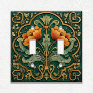 May include: A decorative double light switch cover with an Art Nouveau floral design. The cover features a dark teal background with orange and gold floral accents. The design includes two toggle switch openings and mounting screw holes.