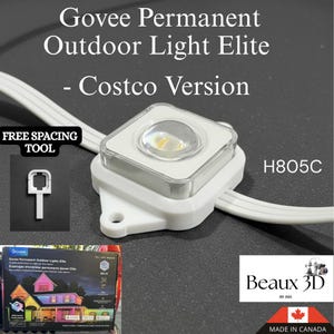 Puede incluir: Primer plano de una luz exterior permanente Govee Elite, versión Costco, de color blanco. La luz tiene forma cuadrada con una lente transparente y una base blanca. El texto "FREE SPACING TOOL" y "H805C" son visibles. También se ve una caja con el logotipo de Govee.