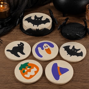 Peut inclure: Un ensemble de cinq dessous de verre ronds en bois avec des motifs d'Halloween incluant un chat noir, un fantôme, une chauve-souris, une citrouille et un chapeau de sorcière, avec un support en forme de chauve-souris et une base Happy Halloween.