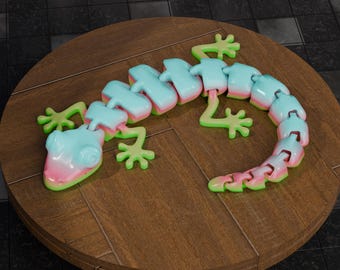 May include: A colorful articulated lizard toy in shades of light blue, pink, and green. The toy is made of connected segments, allowing for flexible movement. It is resting on a round wooden surface.