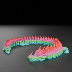 May include: A colorful, articulated dragon toy in shades of pink, orange, green, and blue. The dragon is posed in a curved shape, with a detailed head and spiky spine. The toy is made of plastic and sits on a dark surface.