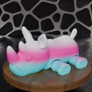 May include: A plush rhino toy in a gradient of colors, including pink, blue, and white. The rhino is lying down on a wooden surface. The background features a metallic, geometric design.