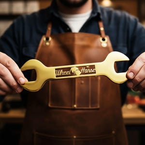 May include: A gold-colored wrench with the text "Wheel Horse" and a horse silhouette. The wrench is held by a person wearing a brown leather apron and a blue shirt. The wrench is a tool.