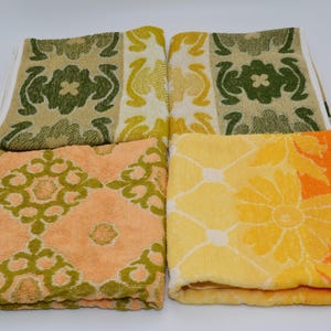 Puede incluir: Cuatro toallas de felpa dobladas con patrones distintos. Dos toallas muestran un motivo floral en verde y beige, una presenta un diseño geométrico en naranja y verde, y la cuarta muestra un patrón floral amarillo y naranja sobre base blanca.