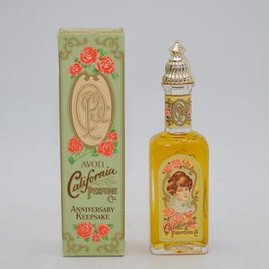 Peut inclure: Flacon et boîte de parfum Avon California Perfume Co. Anniversary Keepsake vintage. Le flacon a un bouchon doré et une étiquette avec un portrait de femme et des roses. La boîte est verte avec des roses rouges et le logo Avon.