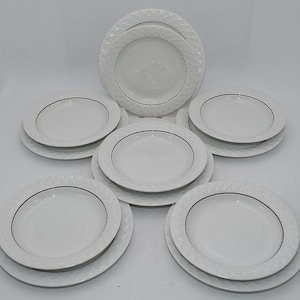 Op de afbeelding: Een witte servies set met meerdere borden van verschillende maten. De borden hebben een ruitpatroon rond de rand en een zwarte rand. De set bevat dinerborden, saladeborden en kommen, allemaal gerangschikt op een wit oppervlak.