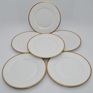 Könnte beinhalten: Sechs weiße Porzellanteller mit einem goldenen Seilrand. Die Teller sind kreisförmig angeordnet und präsentieren ihr elegantes Design. Ideal für formelle Anlässe oder besondere Abendessen.