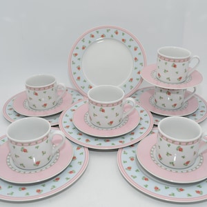 Könnte beinhalten: Vintage Porzellan-Teeservice mit Tassen, Untertassen und Tellern. Das Set hat eine weiße Basis mit einem floralen Muster aus roten Rosen und grünen Blättern. Die Ränder sind mit einem rosa Rand und blauen floralen Akzenten versehen.