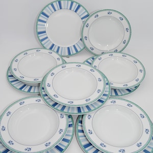Peut inclure: Un ensemble d'assiettes et de bols en céramique blanche. Les assiettes présentent un motif de bordure à rayures bleues et vertes, tandis que les bols arborent un motif floral. L'ensemble comprend différentes tailles d'assiettes et de bols.