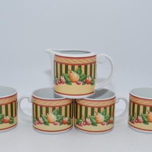 Può includere: Un set di tazze in ceramica e una lattiera con un design a frutta. Le tazze e la lattiera hanno uno sfondo giallo con strisce verticali verdi e un bordo decorativo. Il design della frutta comprende pere, mele e bacche.