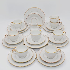 Pode incluir: Um conjunto de chá em porcelana branca com bordas recortadas e acabamento dourado. O conjunto inclui várias chávenas, pires, pratos pequenos e uma leiteira. Cada peça tem um acabamento liso e brilhante com um design consistente.
