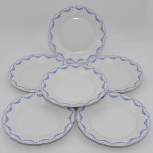 Könnte beinhalten: Sechs weiße Keramikplatten mit blauem Blumenrand und gewelltem Rand. Die Teller sind kreisförmig angeordnet und präsentieren ihr elegantes Design. Jeder Teller hat einen Durchmesser von ca. 20 cm.