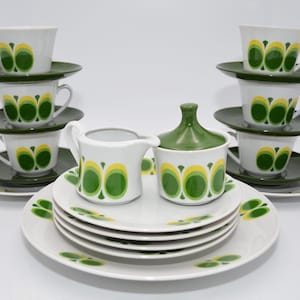 Könnte beinhalten: Vintage weißes Keramik-Teeservice mit grünem und gelbem Blumendesign. Das Set umfasst Tassen, Untertassen, Teller, einen Sahnekännchen und eine Zuckerdose mit Deckel. Die Tassen und die Zuckerdose haben grüne Deckel.