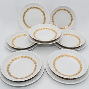 May include: A set of white ceramic dinnerware with a textured surface. Each piece has a gold floral pattern around the rim. The set includes dinner plates, salad plates, and bowls, arranged on a white background.