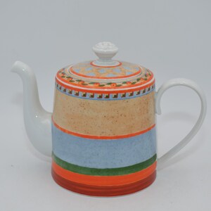 Può includere: Teiera in ceramica bianca con manico e beccuccio curvi. Il corpo presenta fasce orizzontali di colore: arancione, blu, verde e marrone. Il coperchio è decorato con un motivo floreale arancione e blu e un pomello bianco.