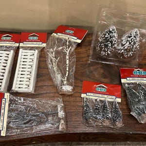 May include: Various Lemax Village Collection miniature decorative items, including white picket fences, snow-covered trees, and dry trees. The items are packaged in clear plastic and have red and white labels.