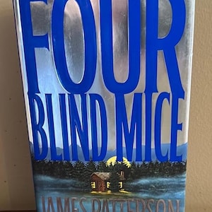 May include: A silver and blue hardcover book with the title "Four Blind Mice" in blue lettering and the author "James Patterson" in silver lettering. The cover features a painting of a cabin in the woods with a full moon in the sky.