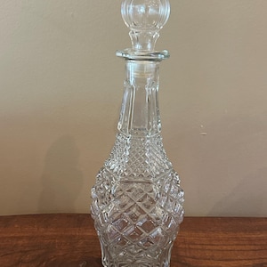 Könnte beinhalten: Eine Karaffe aus klarem Glas mit einem Rautenmuster am Körper, einem verjüngten Hals und einem passenden Glasstopfen mit gerippter, abgerundeter Oberseite. Der Boden der Karaffe ist mit einem Sternmuster versehen und das Glas ist durchsichtig.