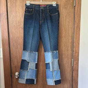 Può includere: Jeans in denim blu scuro con dettagli patchwork sulle gambe svasate. I jeans hanno un classico design a cinque tasche e una chiusura con bottone e cerniera. Il patchwork presenta varie tonalità di denim blu.