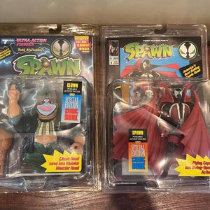 Peut inclure: Deux figurines articulées Spawn de Todd McFarlane dans leur emballage blister d'origine. L'emballage de gauche contient une figurine Clown avec une tête de monstre. Celui de droite contient une figurine Spawn avec une cape rouge et une BD.