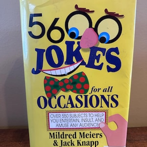 Op de afbeelding: Een geel boek met de titel "5600 JOKES" met cartoonogen, een neus en een lachende mond. Een groene vlinderdas met rode stippen staat onder de mond. De tekst "for all OCCASIONS" staat onder de vlinderdas. Het boek is van Mildred Meiers & Jack Knapp.