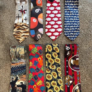 May include: A selection of eight patterned neckties. Designs include crosses, billiard balls, sheep, motorcycles, sunflowers, and Native American patterns. The ties feature a range of colours, from navy to red, with detailed illustrations.